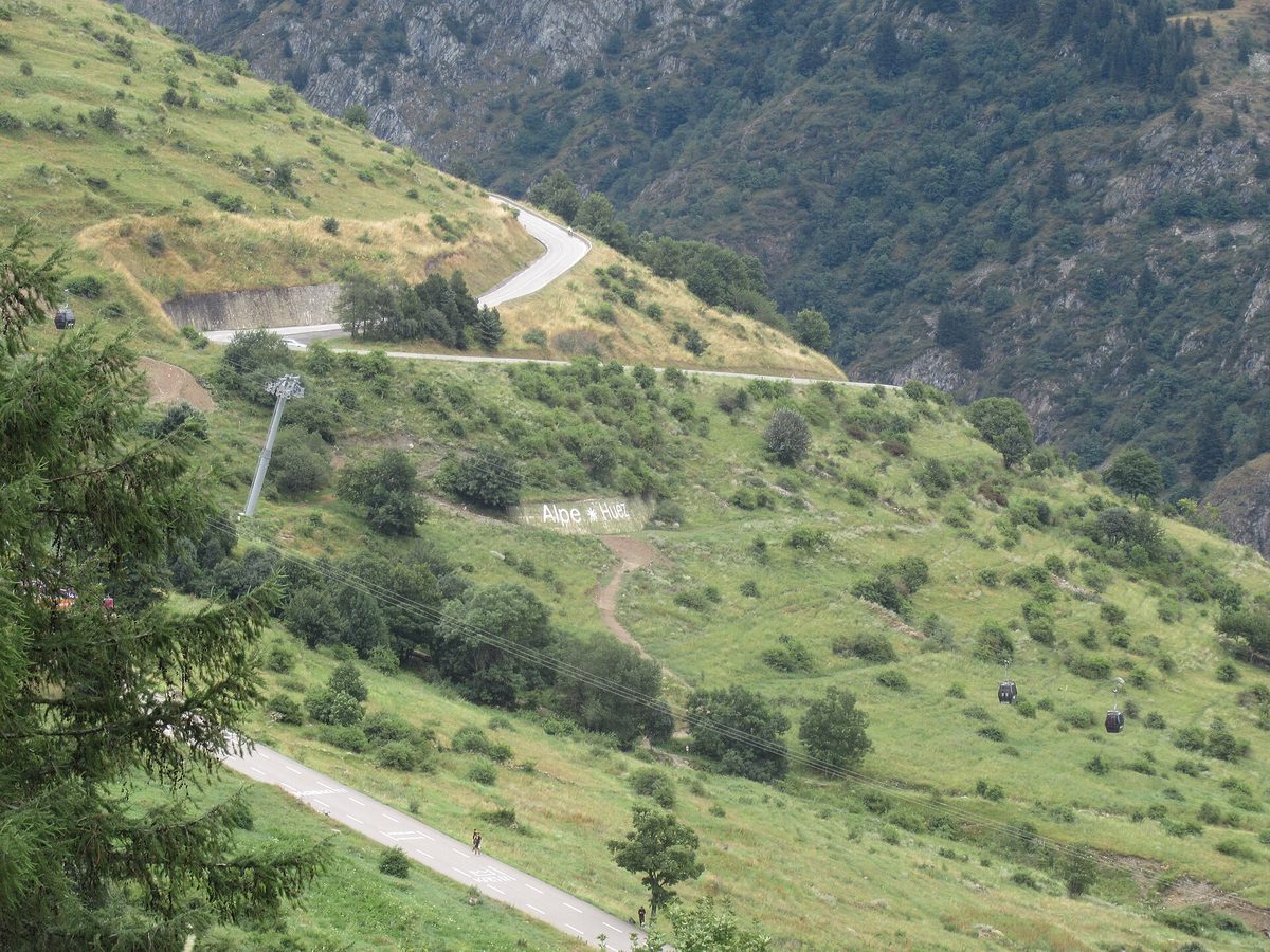 Hairpin bends of the Alpe d'Huez road climbing a green mountainside, during the Tour de France Femmes 2024