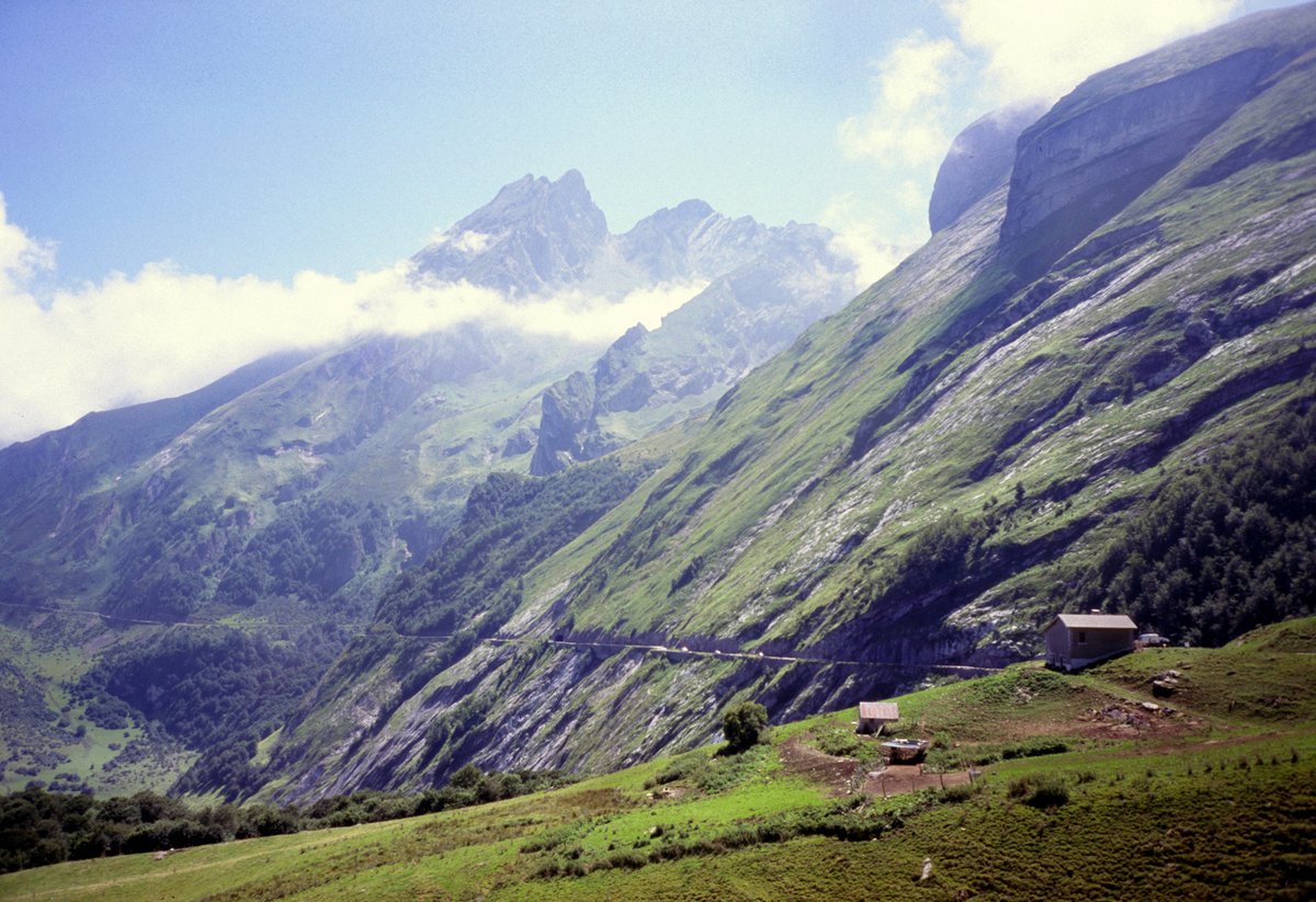 The narrow road from the Col d'Aubisque to the Col du Soulor cut into the cliffs of the Cirque du Litor, with green pastures in front and jagged peaks behind